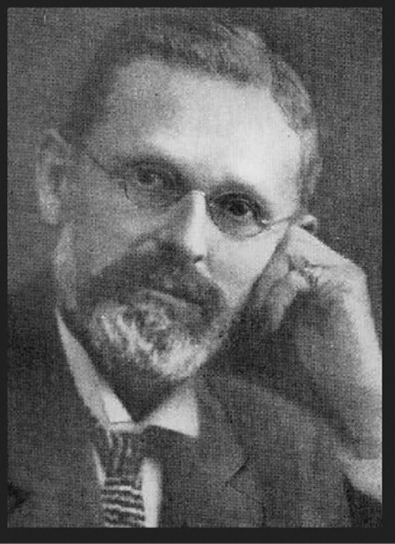 Headshot photograph of a bespectacled man in a suit and tie.