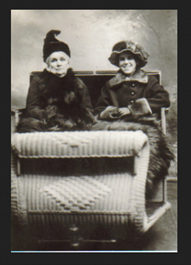 Two women pose on a sleigh in a photography studio.