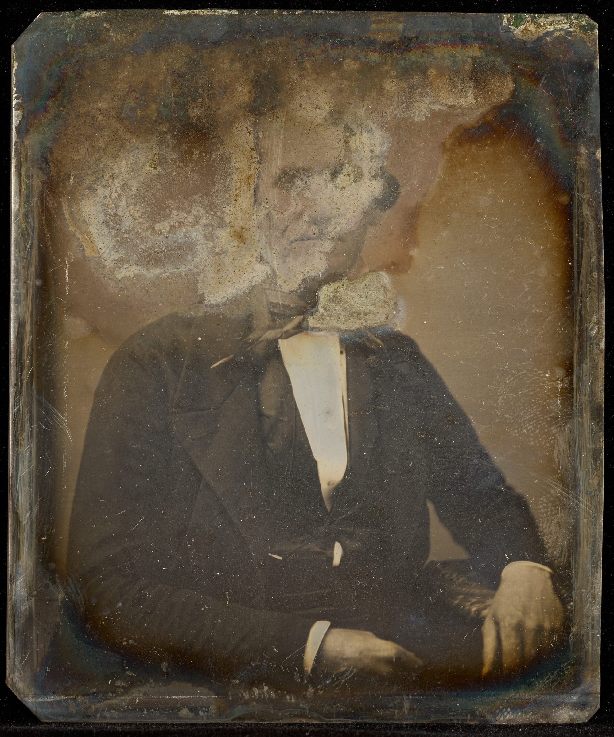 An old portrait photograph in poor condition, with the man's face largely obscured by deterioration.