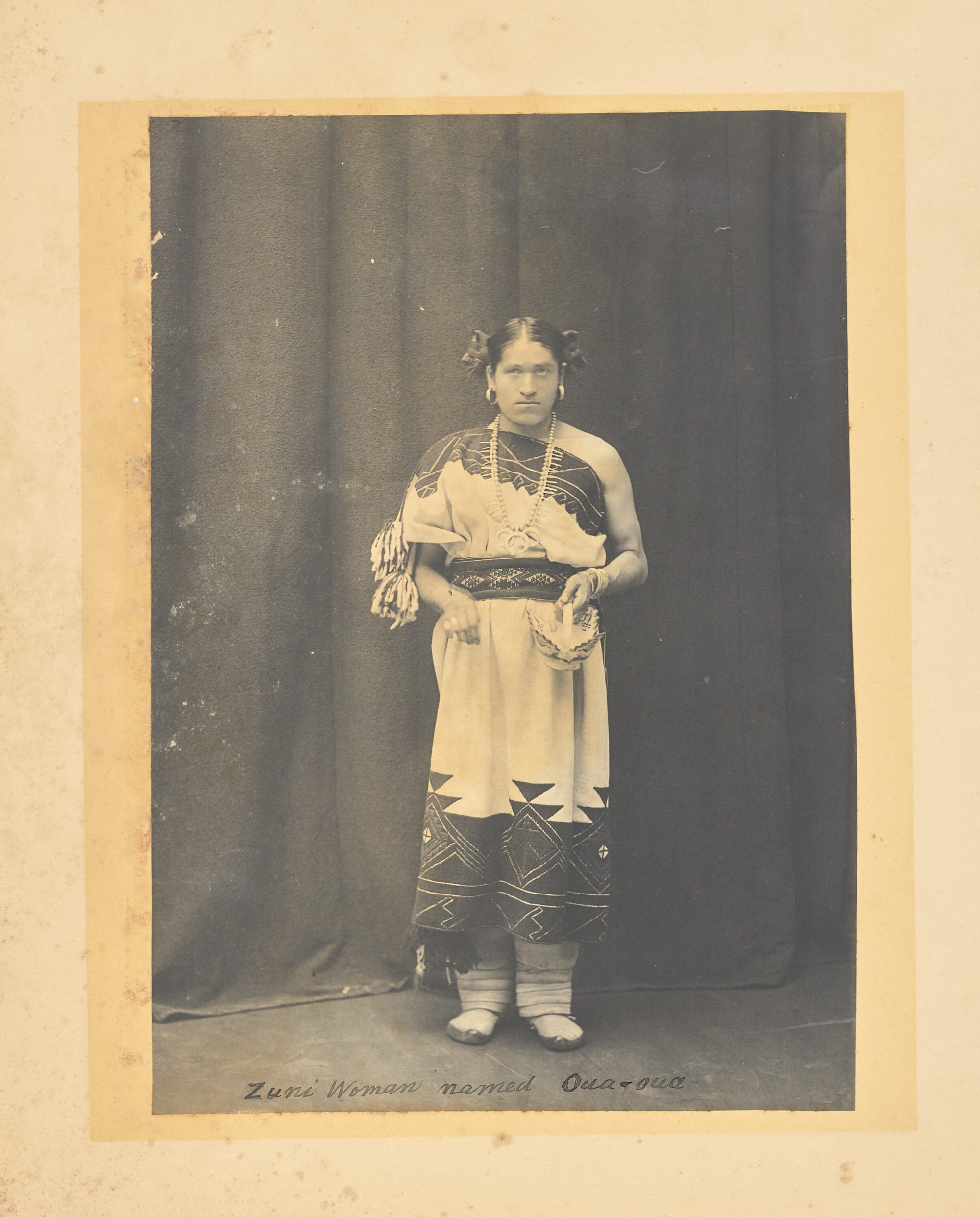 An faded black & white photograph of an Indigenous person dressed in native garb.