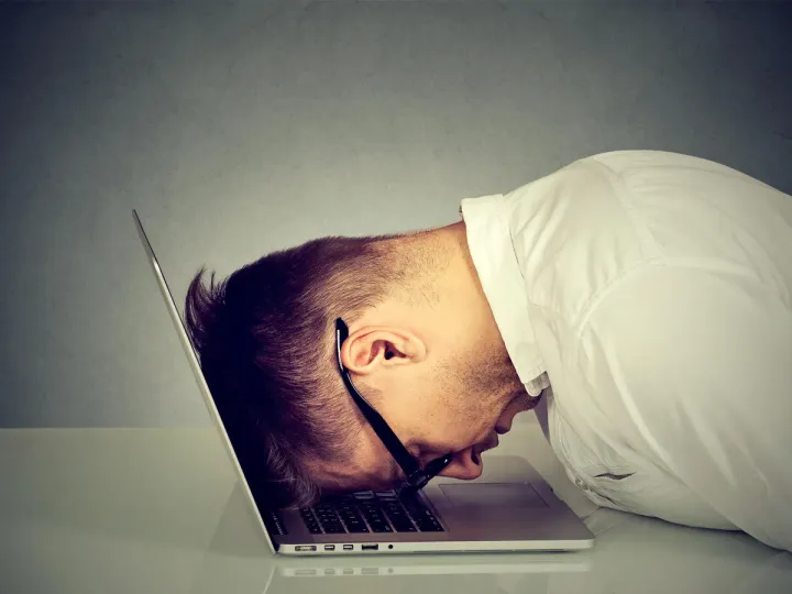 A man bangs his head into a laptop keyboard.
