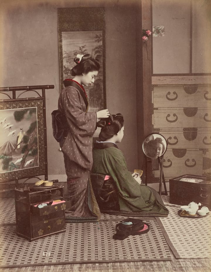 Late 19th C. photo of two Japanese women in traditional dress and home setting, with one (standstyling the hair of the other.