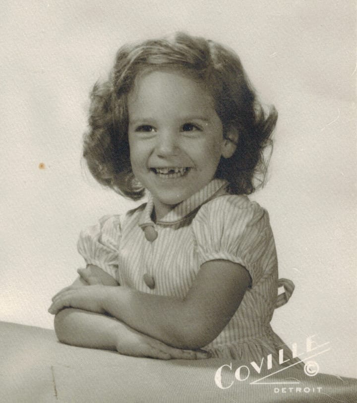 Portrait studio photograph of a young girl, smiling with a tooth missing. 