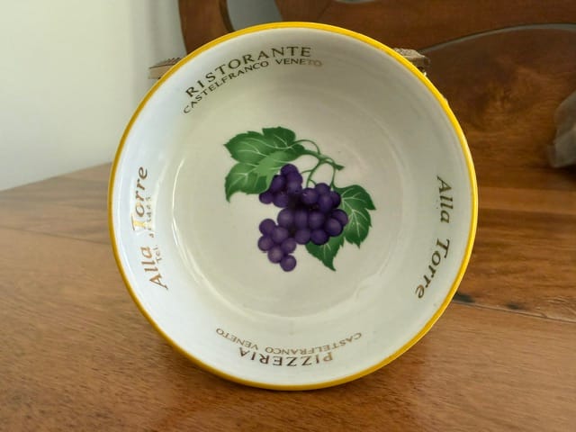 A porcelain ashtray, white ground, with gilt edges, purple grapes, green leaves and brown stems, and gold lettering.