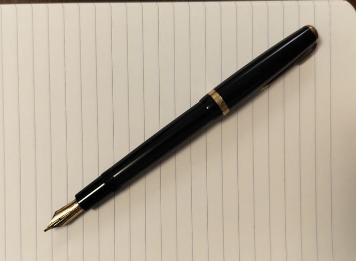 A fountain pen sits atop a pad of lined paper.