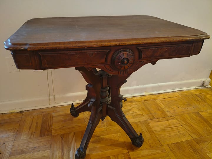 A Victorian parlour table made of black walnut in the Eastlake style, with burled veneer panels, ornately carved medallions, and finials upon its legs splayed out from a centre spindle.
